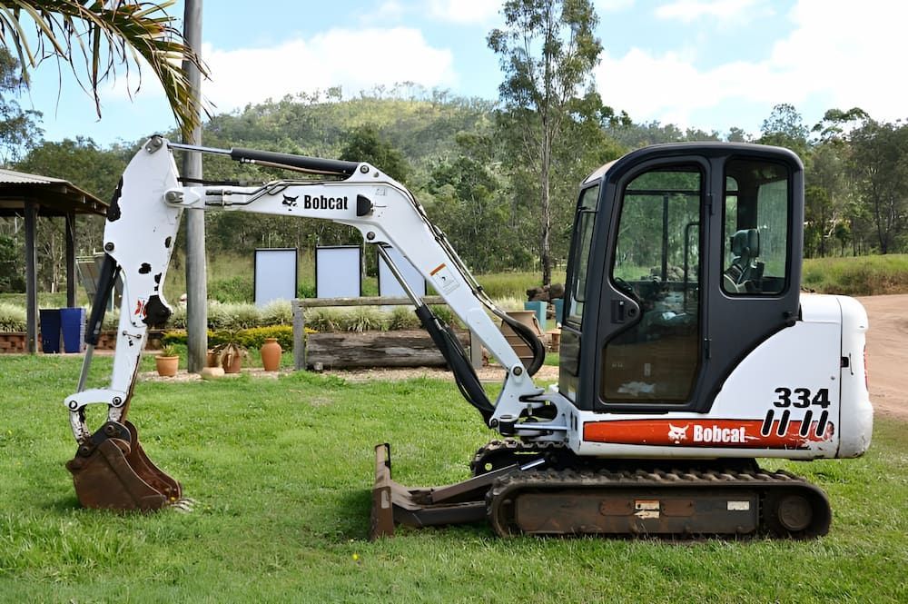 A Bobcat Excavator Is Parked In A Grassy Field — S & K Raw Materials & Earthmoving in Atherton, QLD