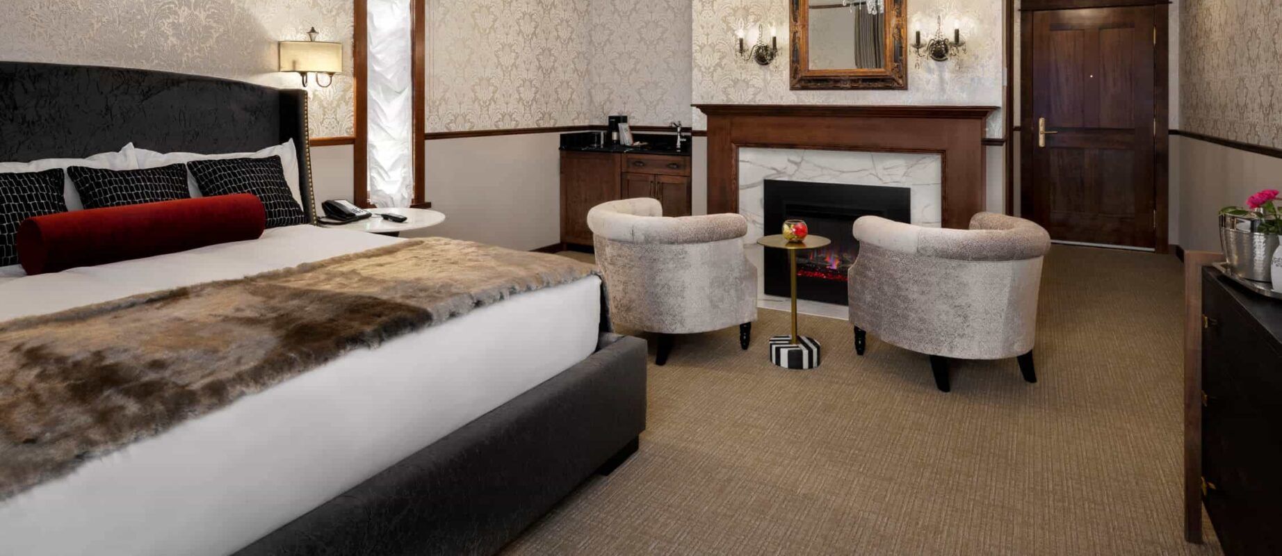 A hotel room with a king size bed , chairs and a fireplace.