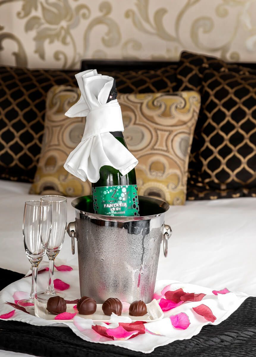 A bottle of wine is in a bucket on a bed