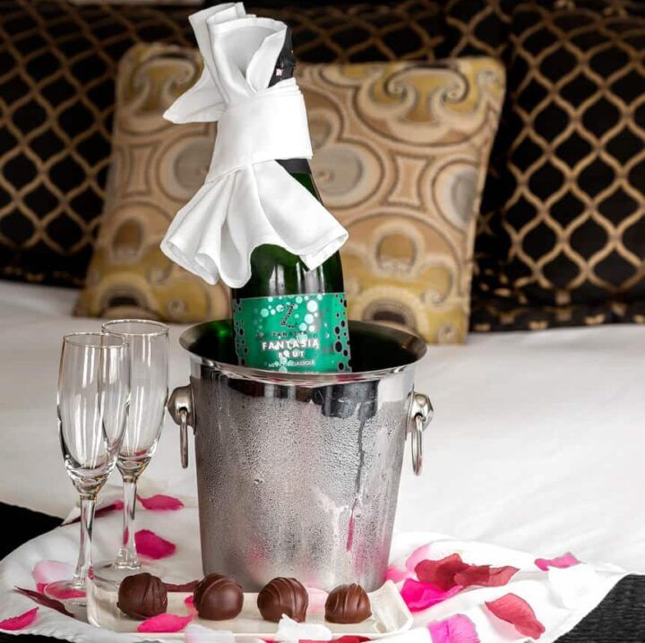 A bottle of champagne in an ice bucket on a bed