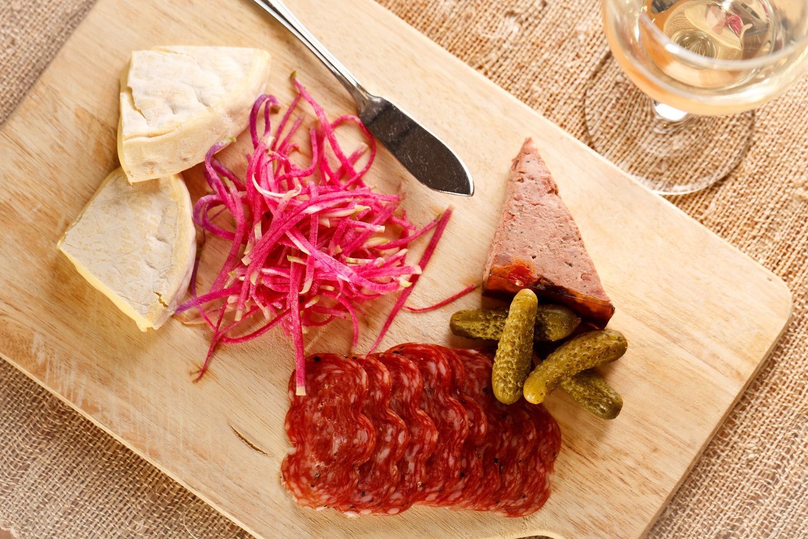 A wooden cutting board with a variety of food and a glass of wine