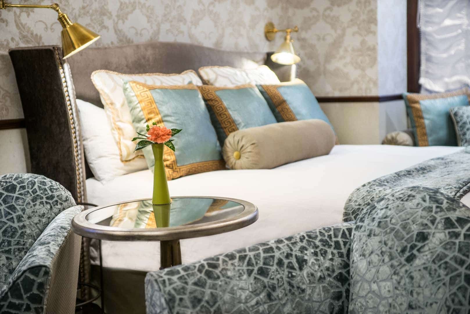 A hotel room with a bed , chairs and a table with a vase of flowers on it.