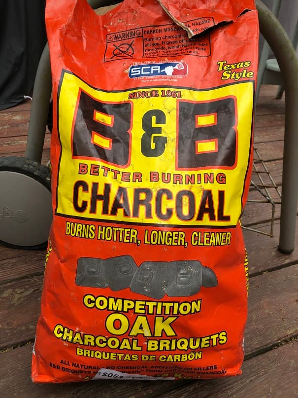 Opened bag of B&B Competition Oak Charcoal Briquets leaning against a weber grill