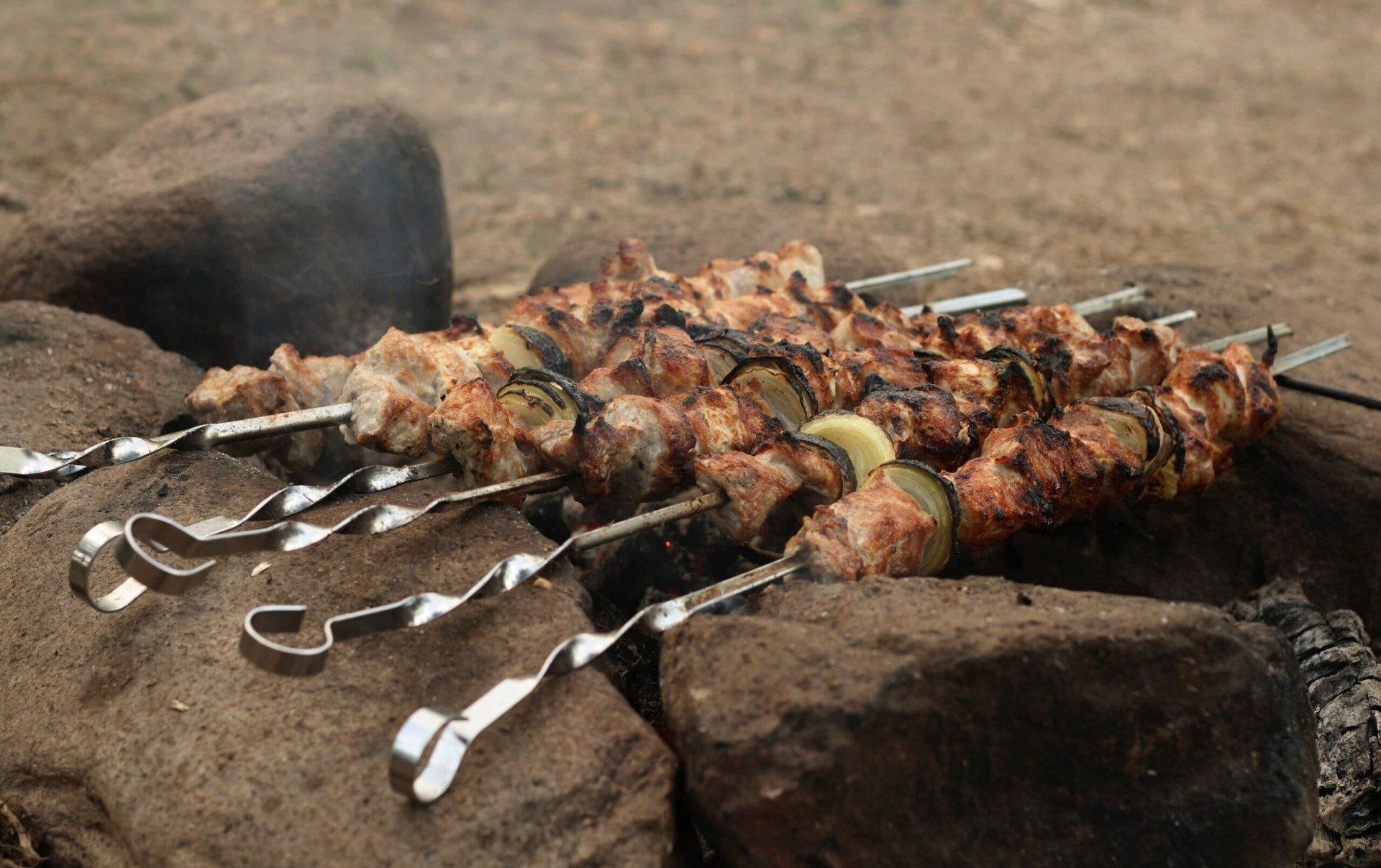 barbecue skewers cooking over a live fire in a rock pit