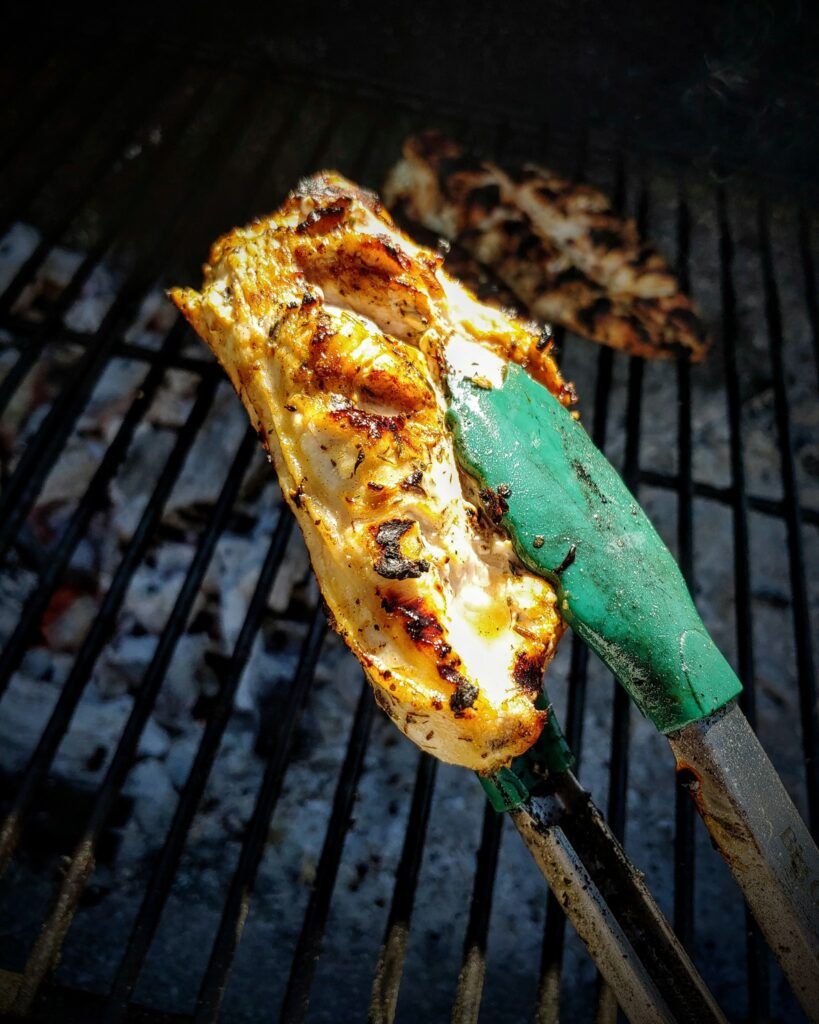 Green Tongs flipping chicken on a BBQ grill