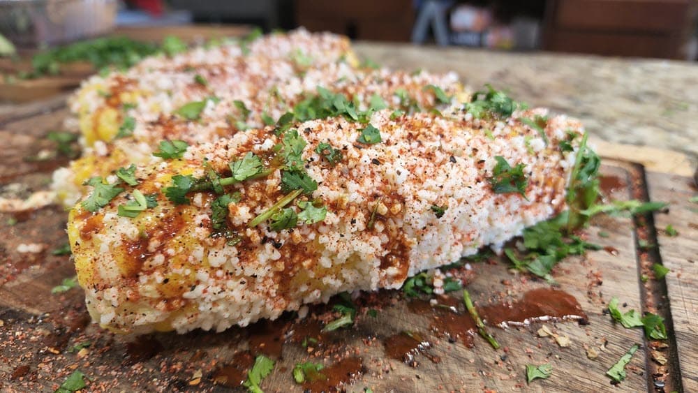 grilled and seasoned corn on the cob on a cutting board