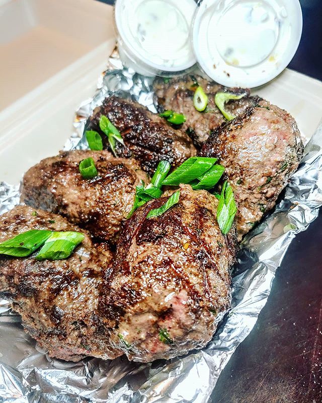 Grilled Angus Sirloin Beef Kofta on foil on plate with side of sauce garnished with green onions