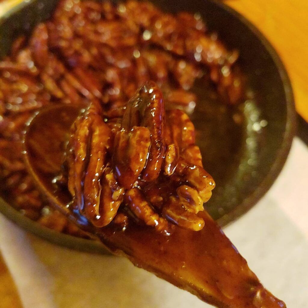 Closeup maple pecans on wooden spoon with skillet of maple pecans in background