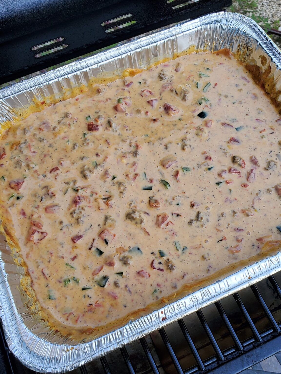 tray of queso with peppers and tomatoes in a pan on the grill