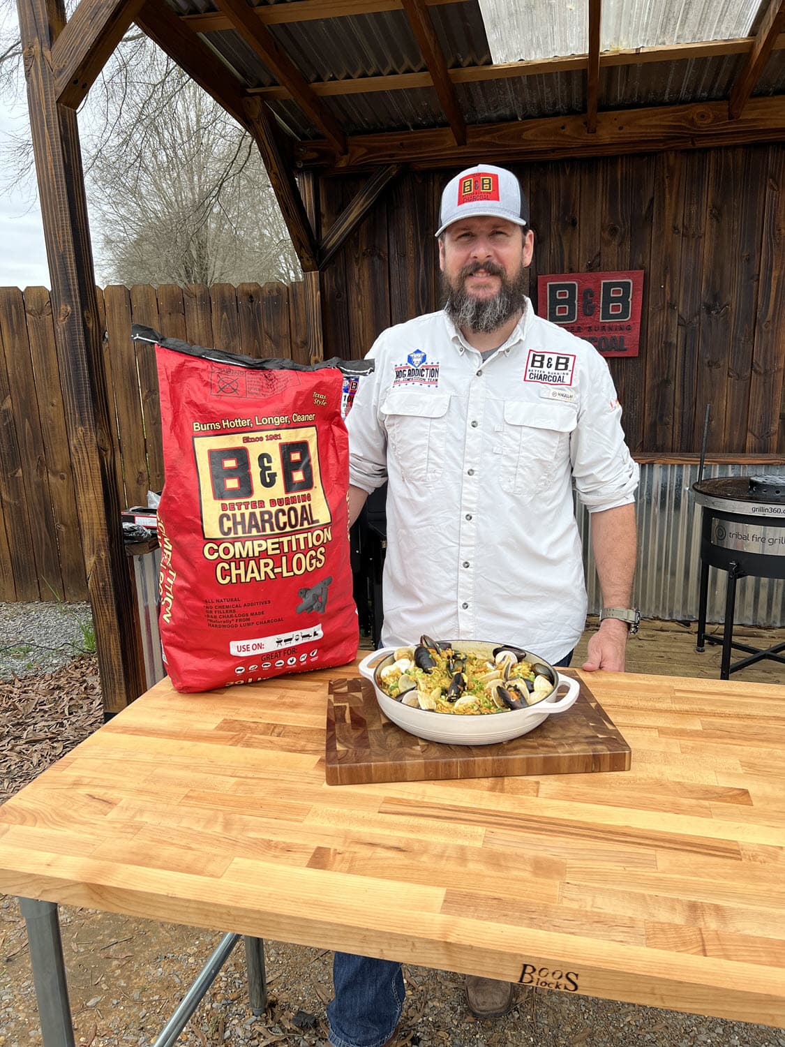 Pitmaster Marcio Borguezan with bag of B&B Competition Char-Logs and grilled seafood paella