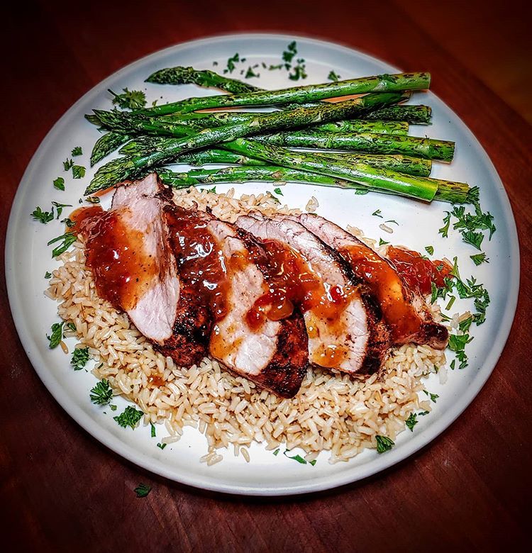 Sliced grilled pork loin on a bed of rice with asparagus on a plate