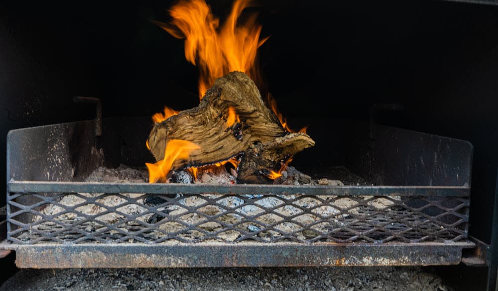 post oak mini logs ablaze in a smoker grate