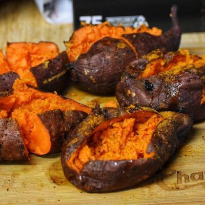 Five grilled sweet potatoes opened on top of a wooden cutting board