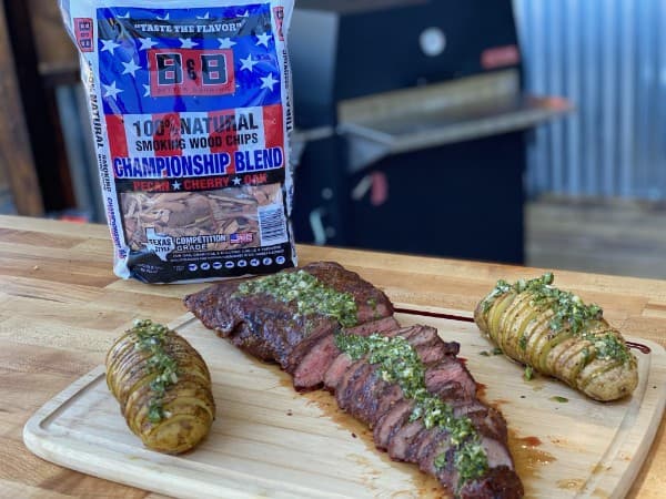 Sliced tri tip and potatoes on a cutting board with a bag of B&B championship blend wood chips