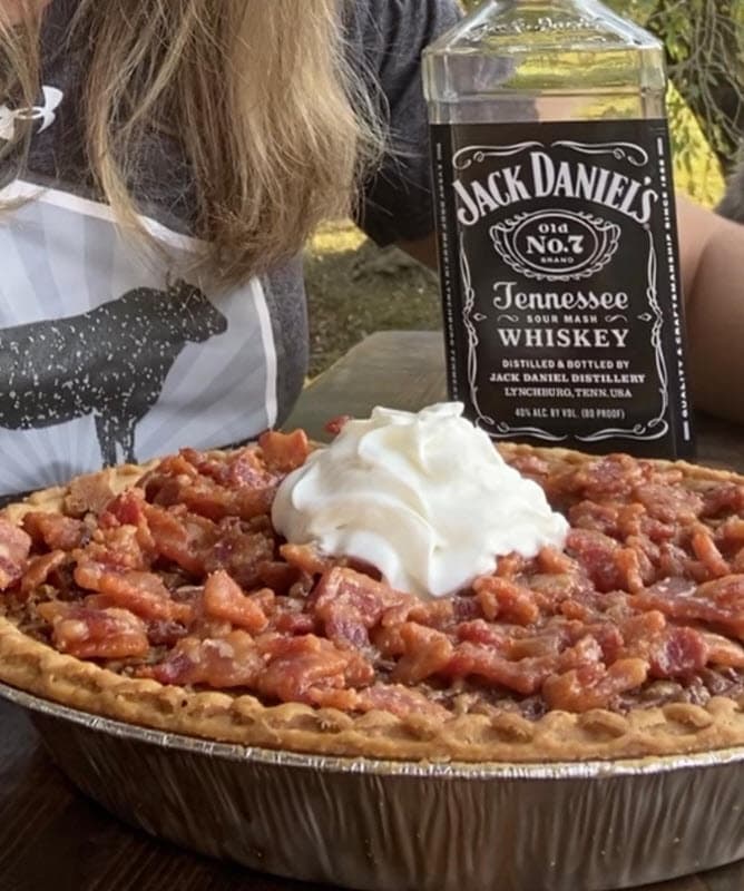 Whiskey Maple Bacon Pie with whipped cream with a bottle of Jack Daniel's Whiskey in the background