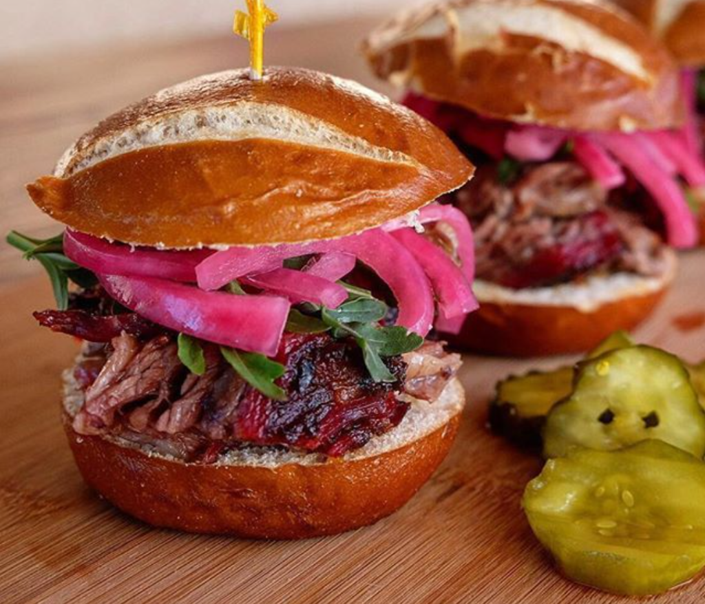Sliced beef with pickled red onions and arugula on a bun with pickles on the side