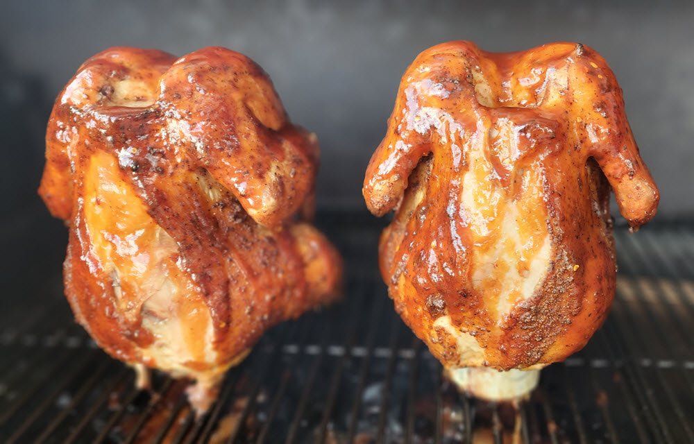 Two whole roasted seasoned chickens cooking on beer cans on the grill