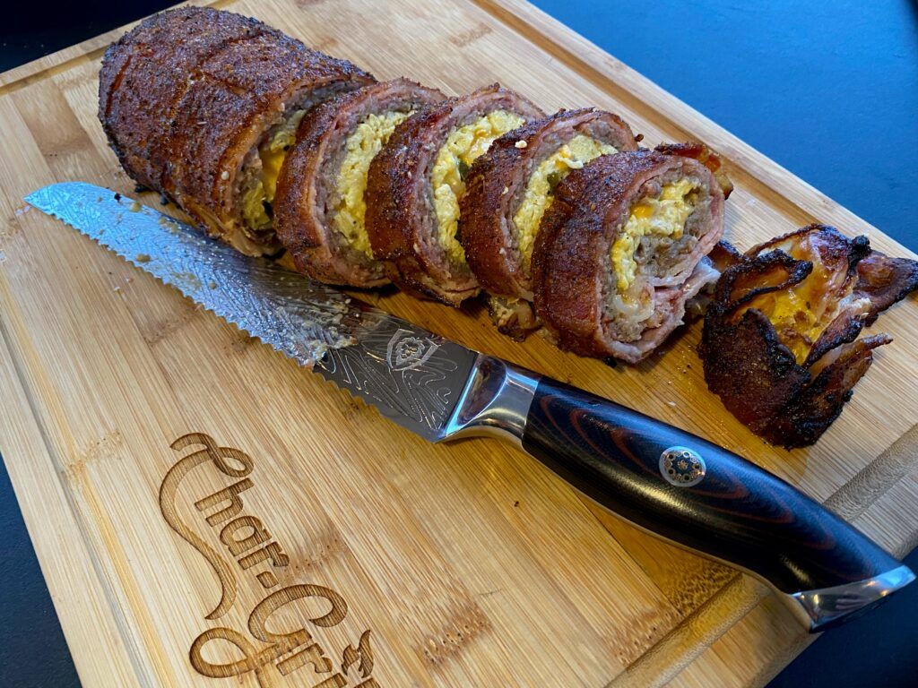 Bacon wrapped egg and sausage rolled, grilled and sliced on a cutting board with a knife