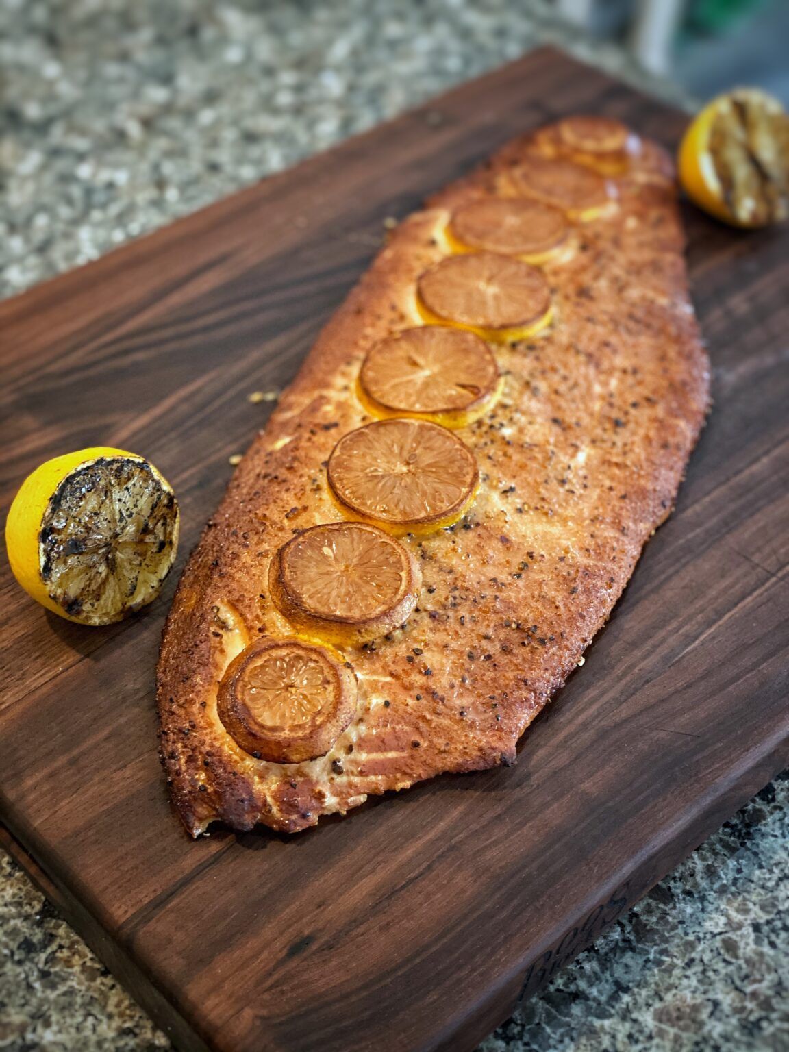 Whole grilled & smoked salmon garnished with lemons on a cutting board