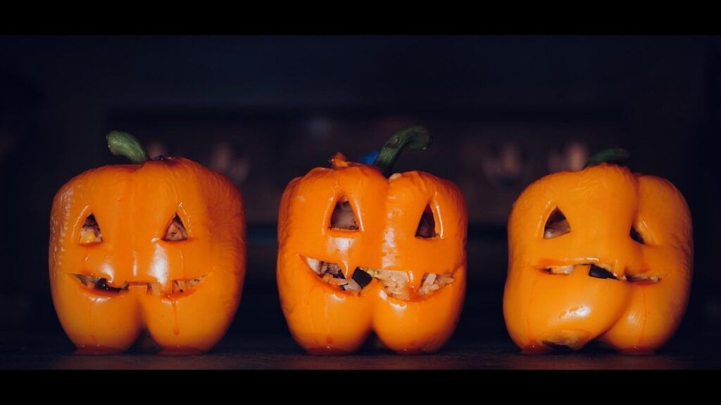 3 stuffed orange bell peppers with halloween faces carved on the front