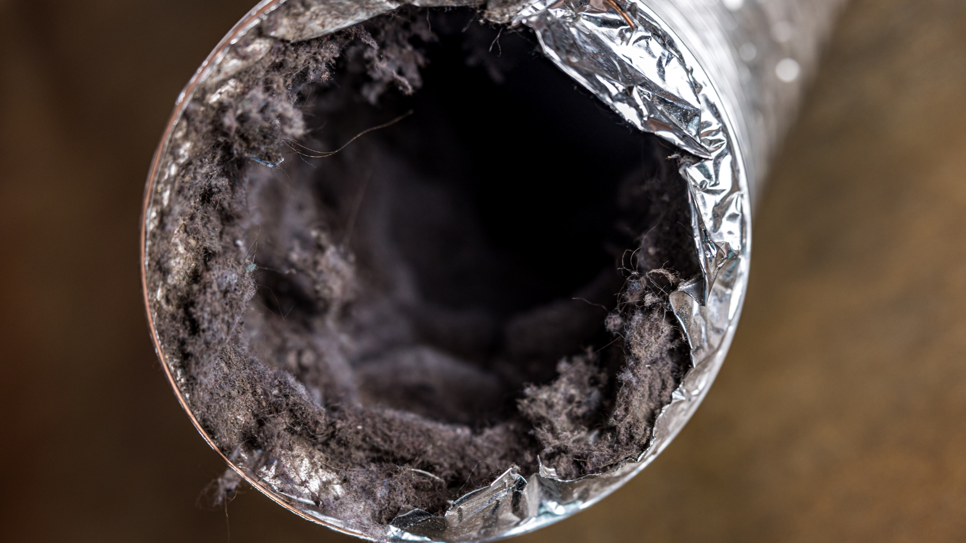 Close-up of a dirty, lint-filled dryer vent. Gray and black debris clogs the metallic tube.