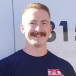 A man with a mustache is smiling in front of a white van.