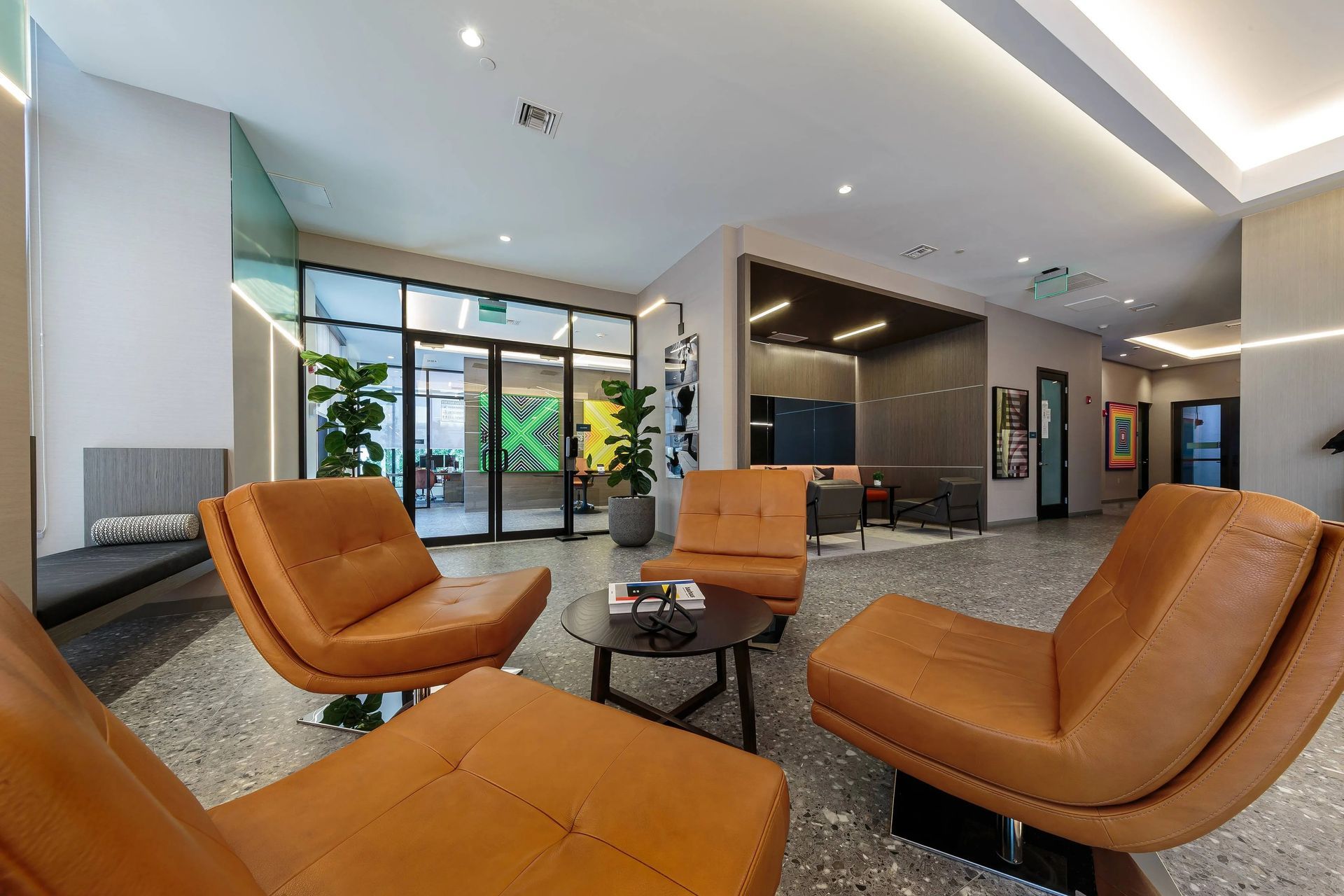 Lounge area with orange chairs, small table, and entrance with greenery.