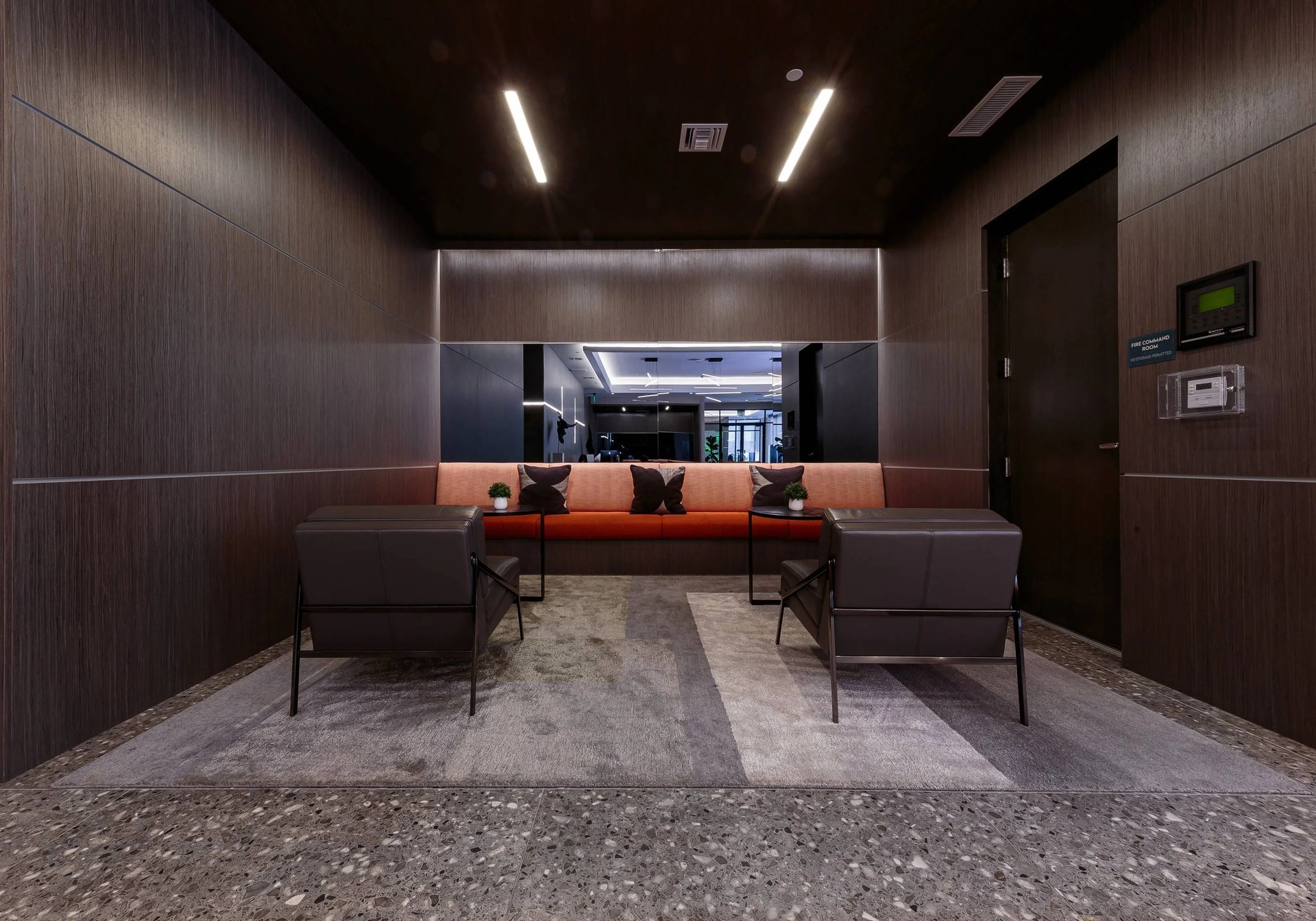 Modern waiting area with dark wood paneling, bench, two chairs, and terrazzo flooring.