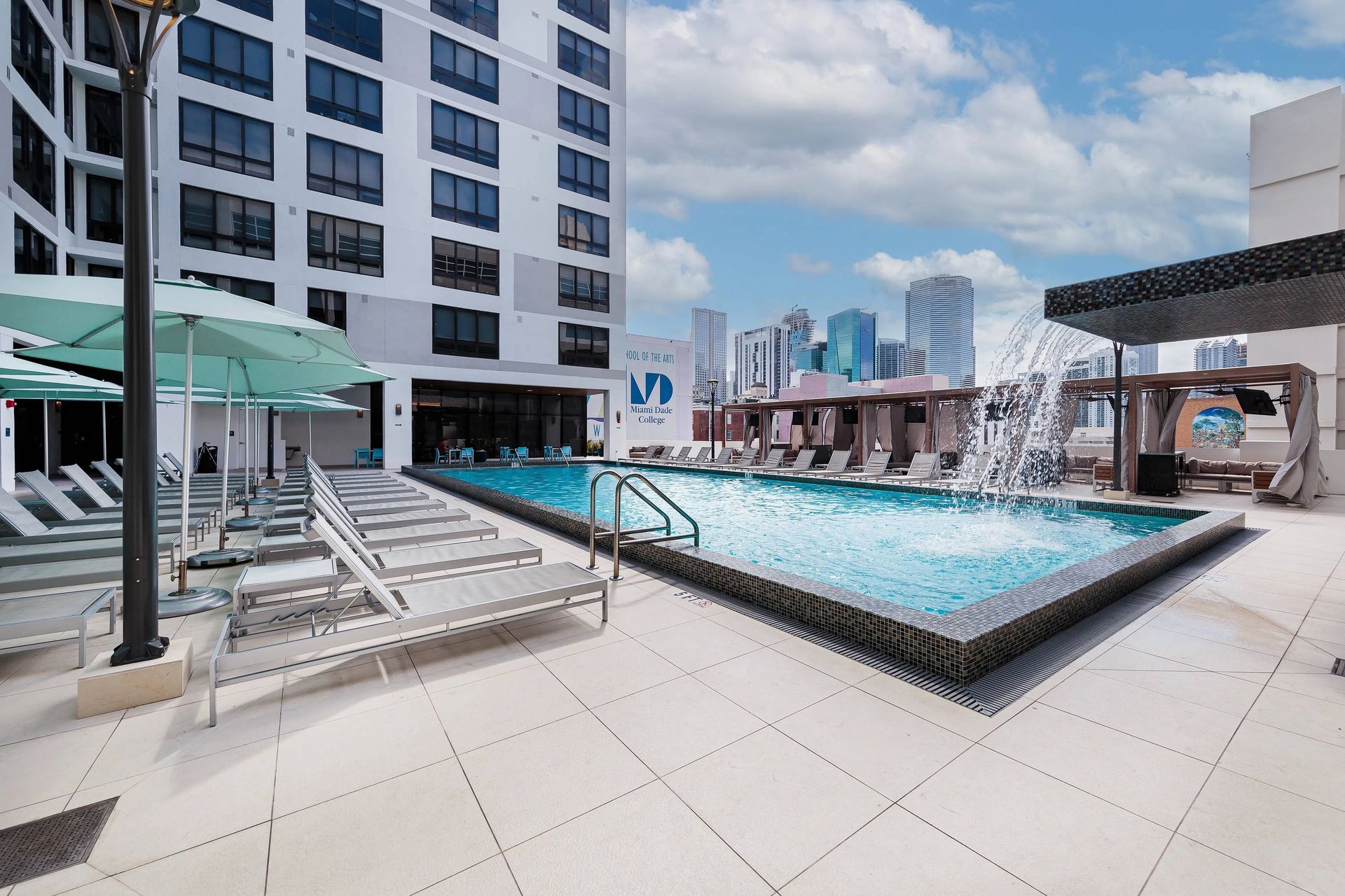 Swimming pool on a rooftop patio with lounge chairs, umbrellas, and city skyline views.