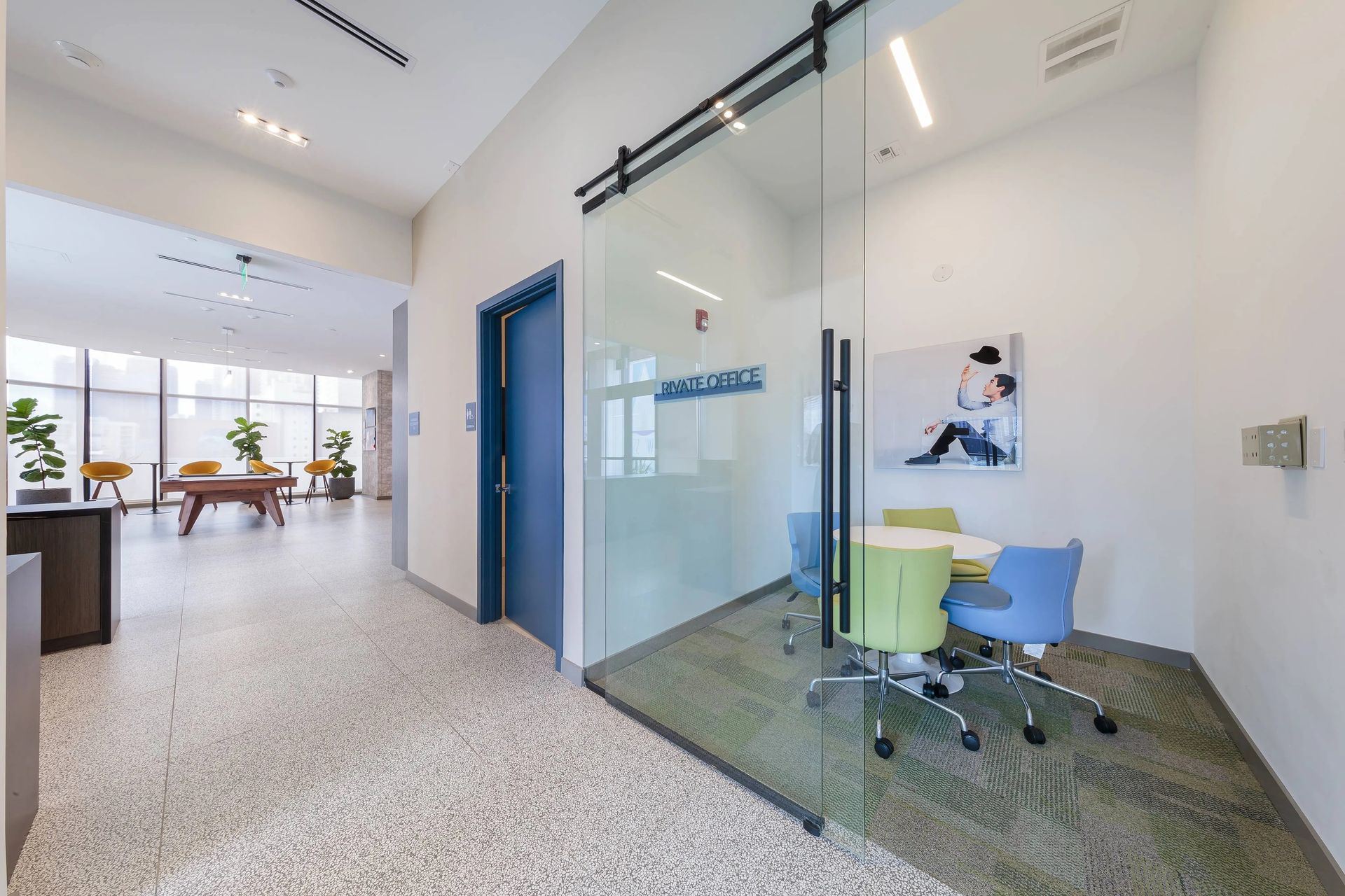 Hallway with meeting room behind glass door, seating, and colorful chairs.