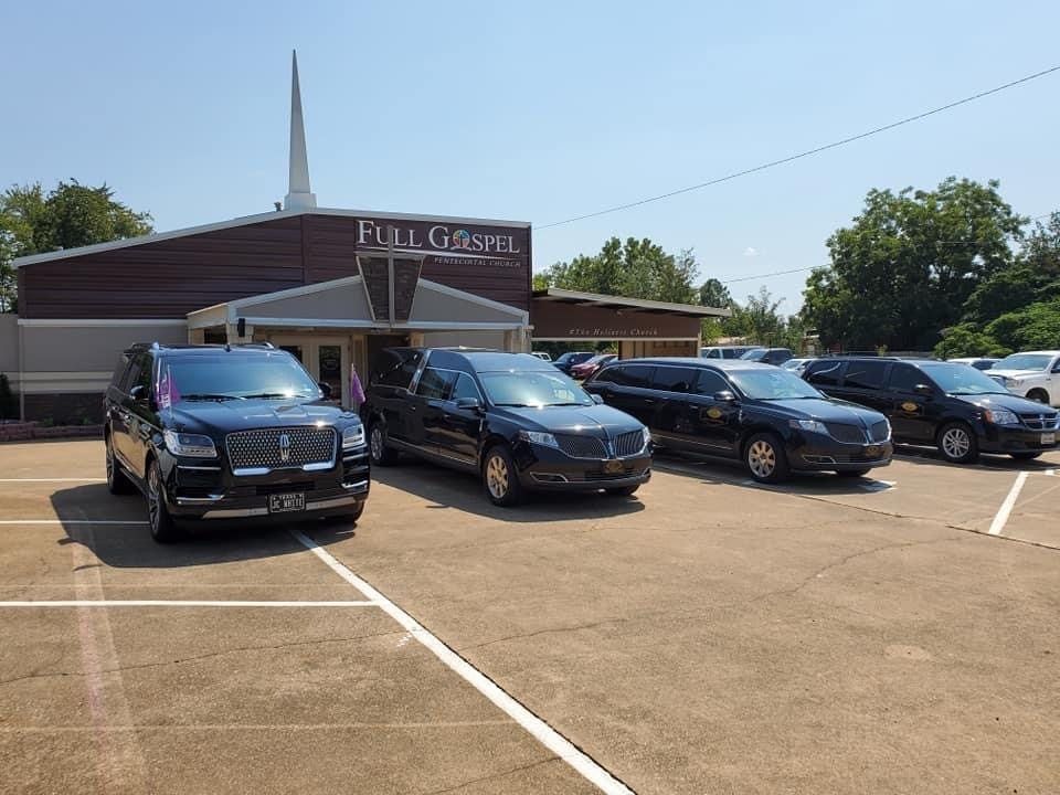 Black hearse vehicles parked in front of a Full Gospel church on a sunny day.