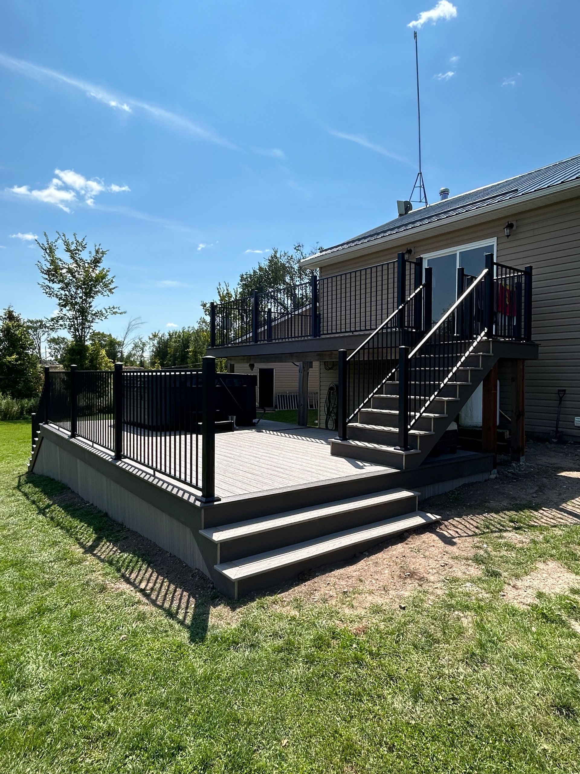 A two-level residential deck with gray composite decking, black metal railings, and a hot tub on the lower level.