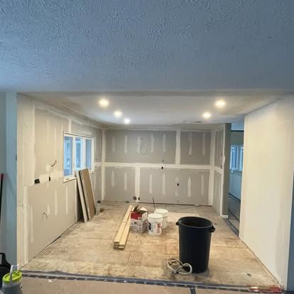 Interior renovation of a room with drywall installed.  Ceiling lights, paint buckets, and tools are visible.