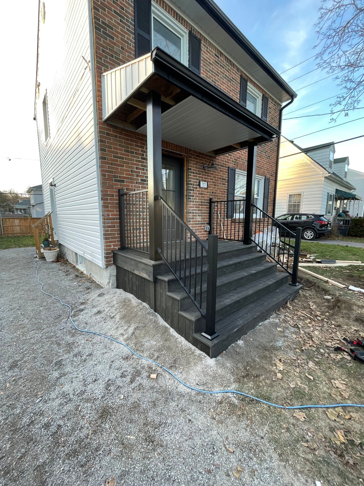Exterior view of a two-story brick building with a dark gray porch and steps; black railings. Gravel and grass are in the yard.