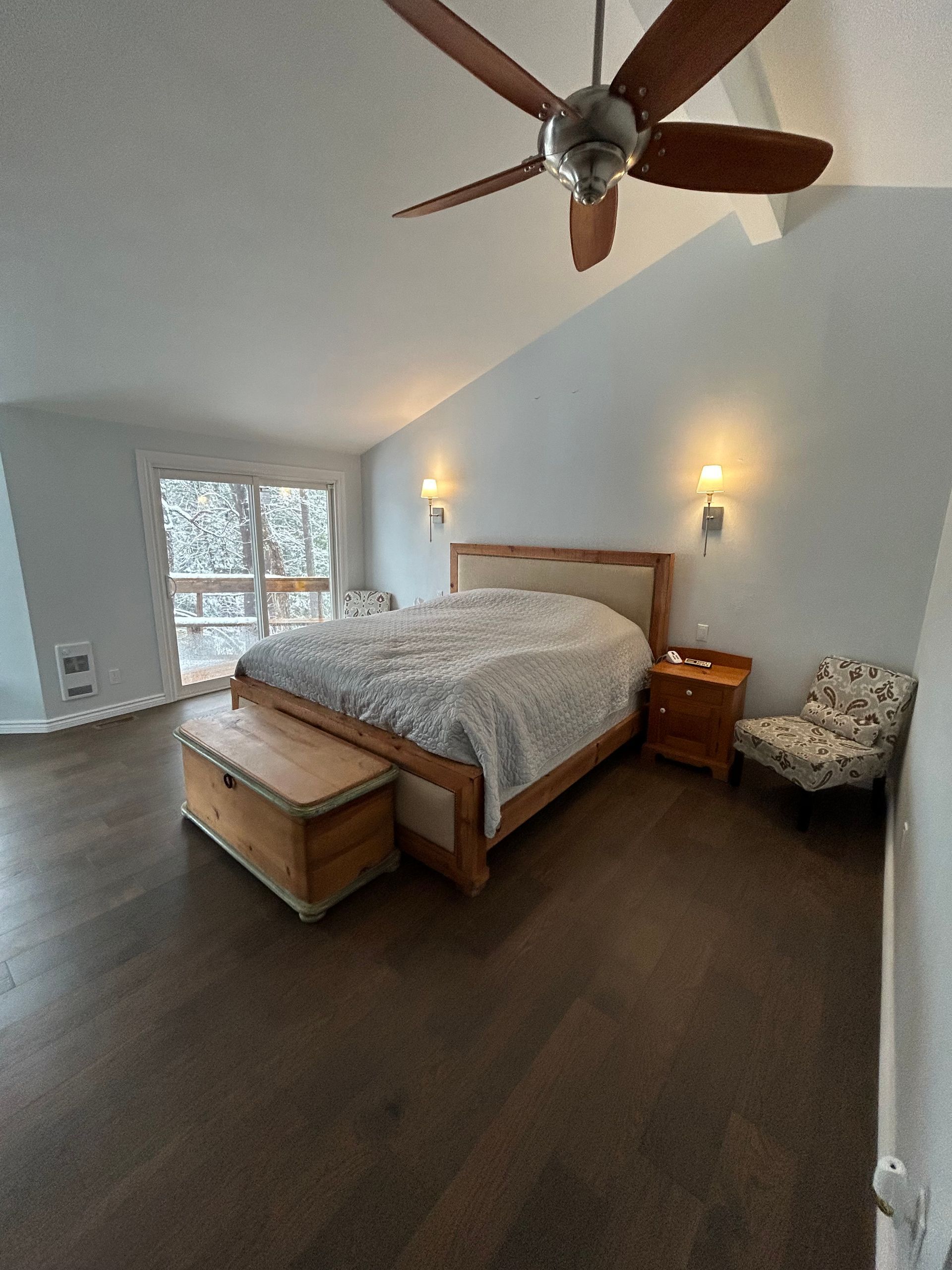 A bedroom with a bed , nightstand , chair and ceiling fan.