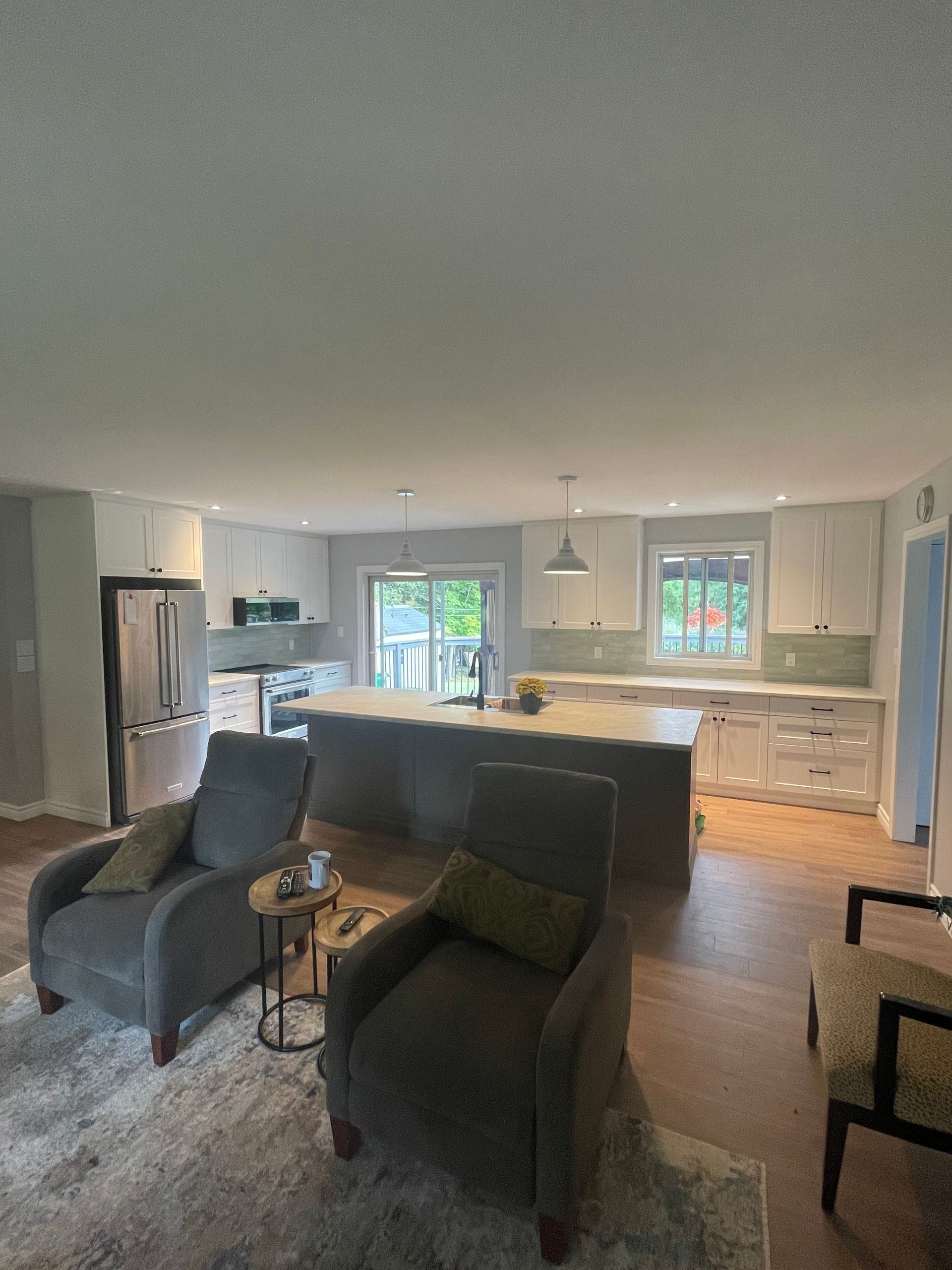 A living room with two chairs and a couch and a kitchen in the background