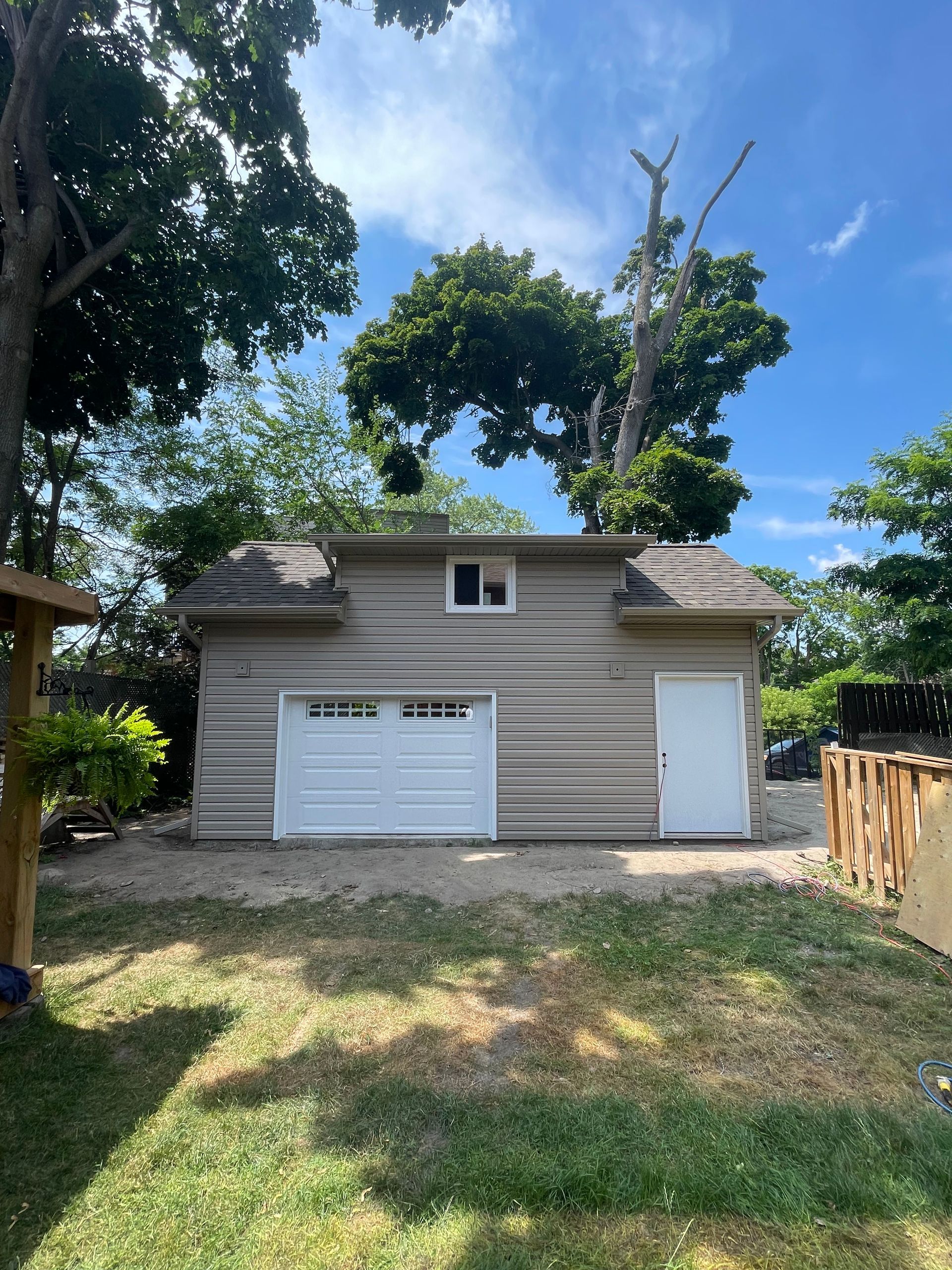 A garage with a white door is in the backyard of a house.