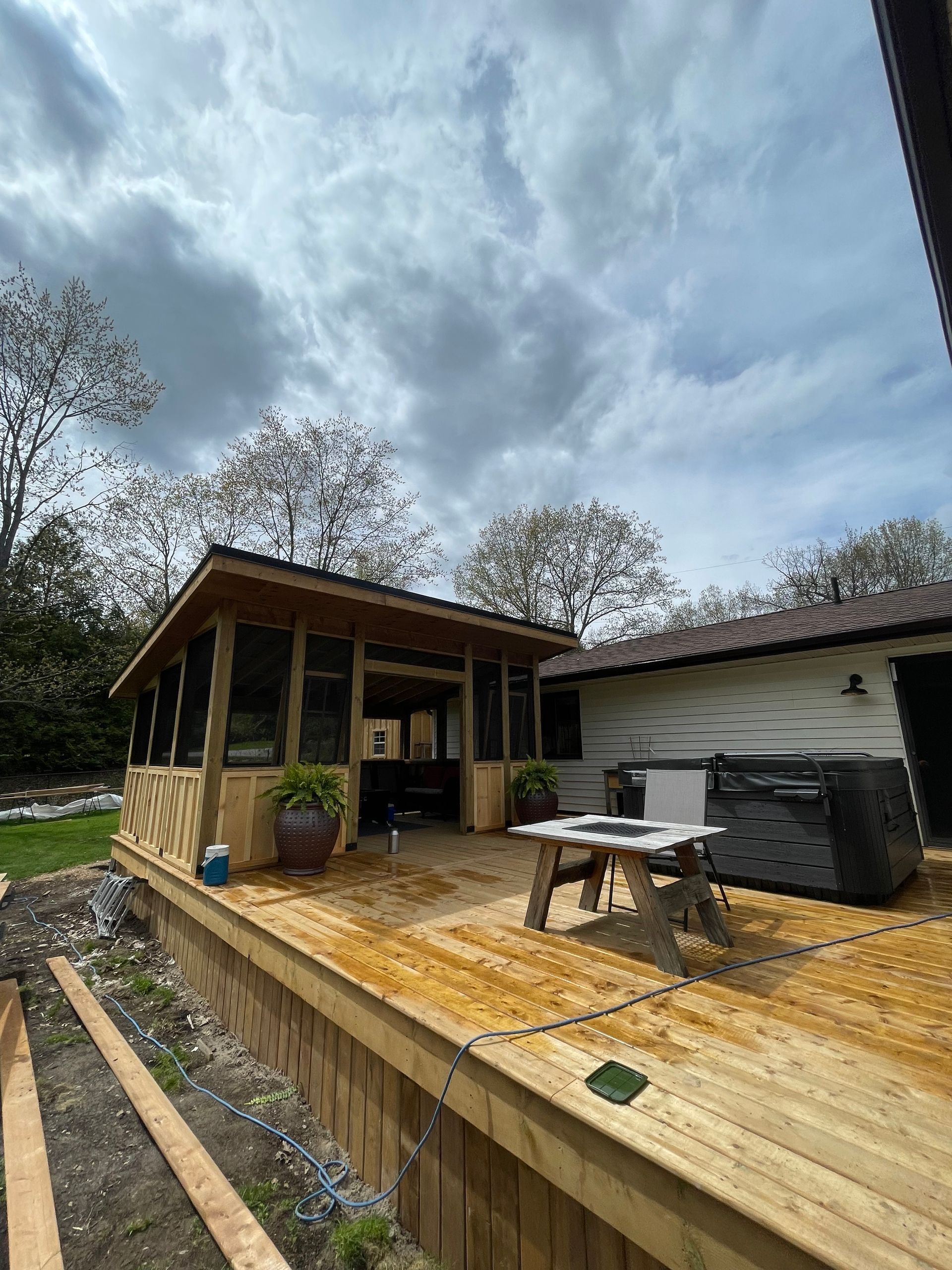 A wooden deck with a gazebo and a hot tub in front of a house.