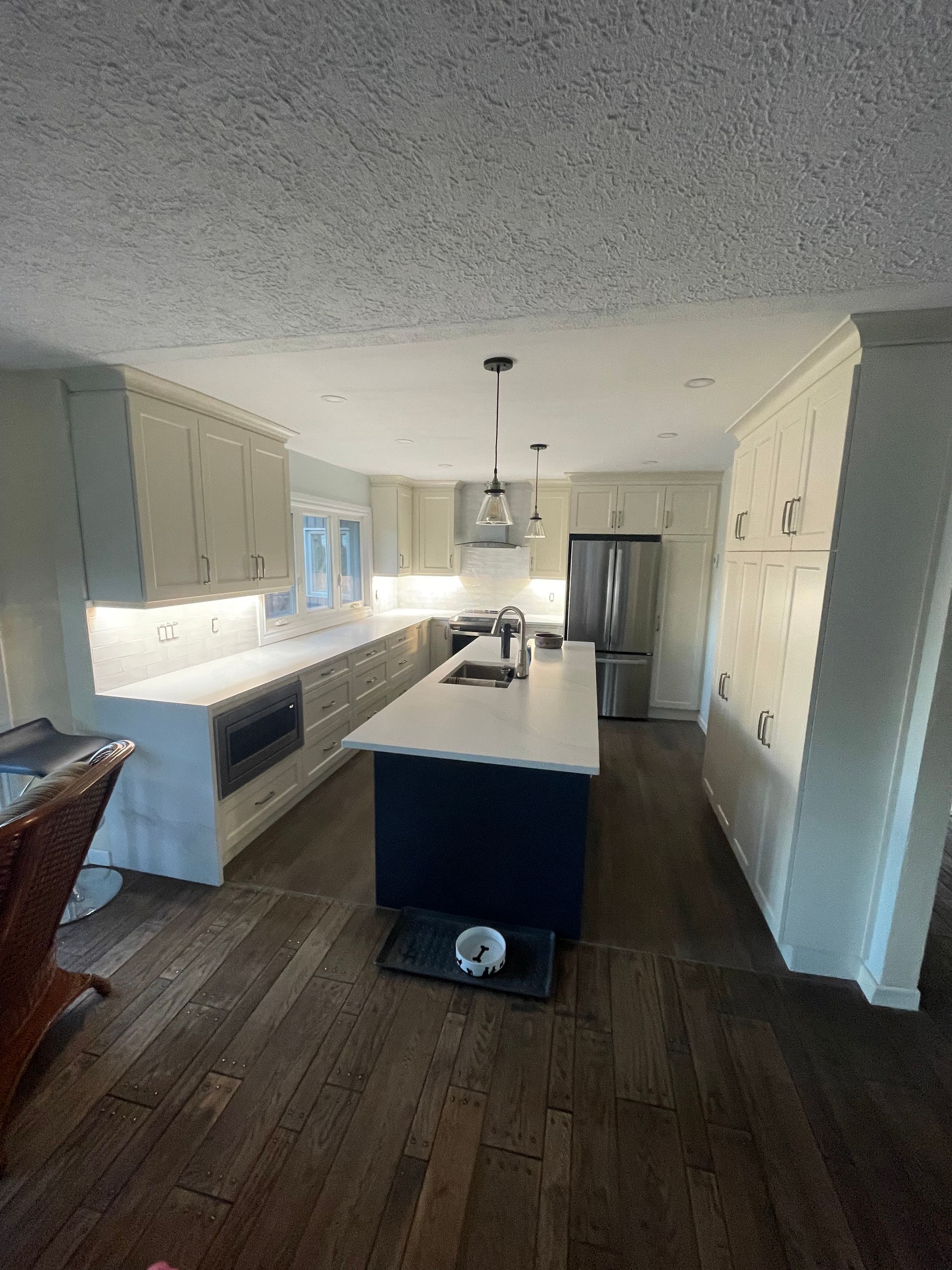 Modern kitchen with white cabinets, dark wood floors, central island, and stainless steel refrigerator