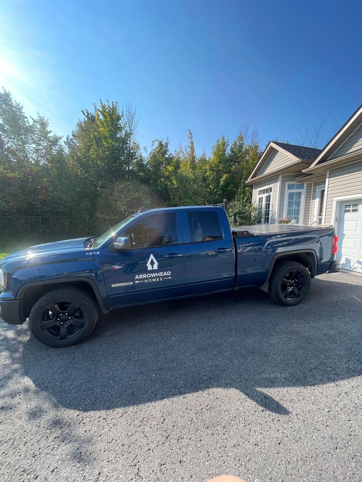 Blue pickup truck parked in a gravel driveway beside a house on a sunny day