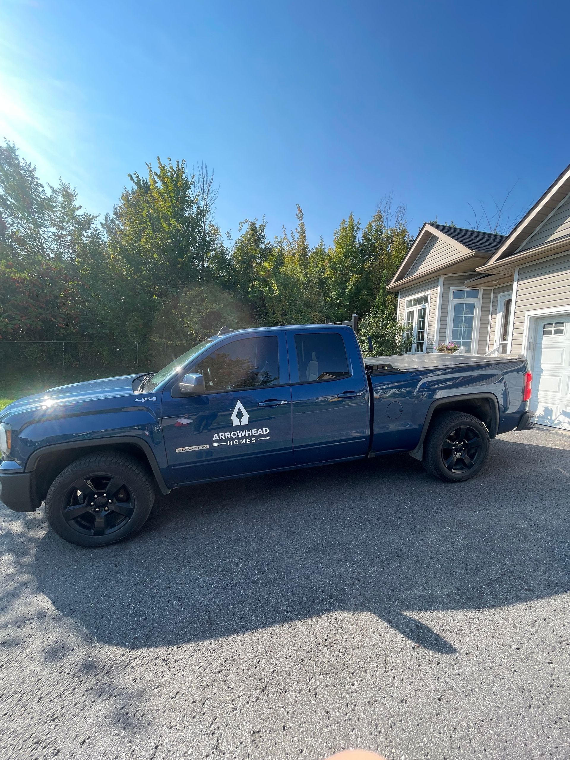 Blue pickup truck parked in a gravel driveway beside a house on a sunny day