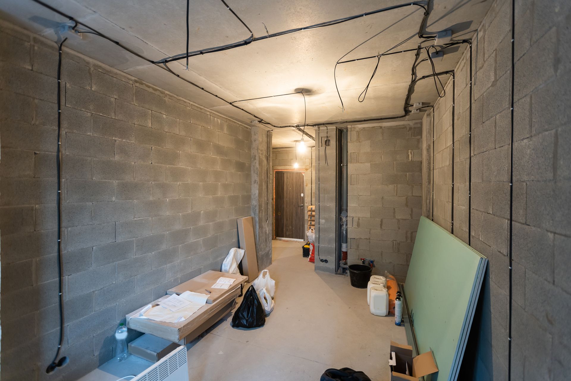 A basement with brick walls and electrical wires hanging from the ceiling.
