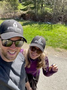 Two people wearing matching hats smile outdoors on a sunny day.