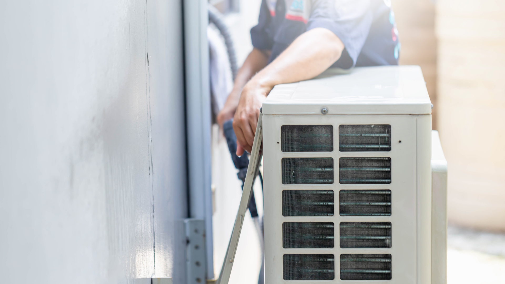 A man is installing an air conditioner on the side of a building.