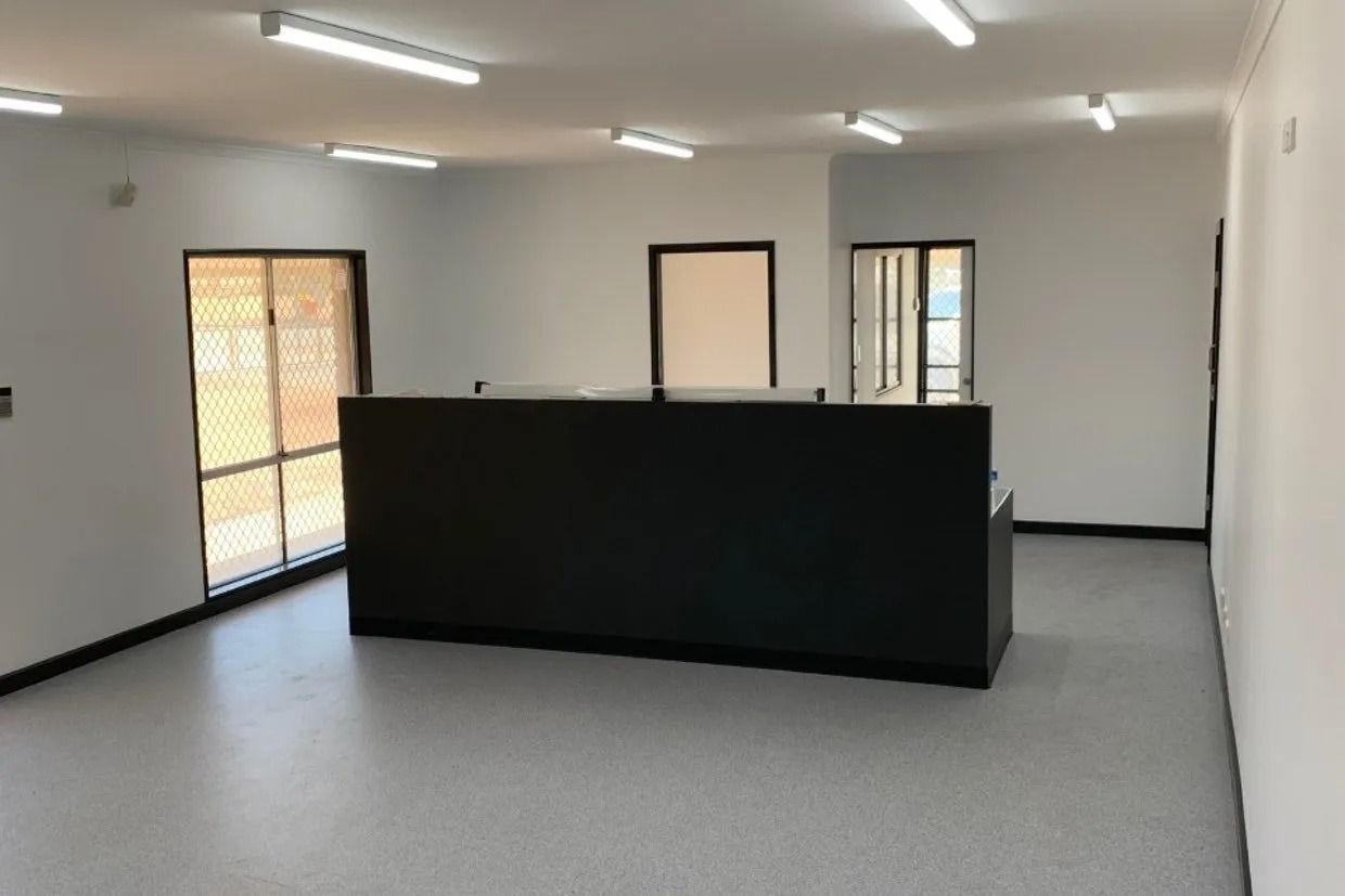 Empty Room With a Large Black Counter, White Walls, Grey Floor, and Exterior Doors — Ozwide Flooring In Ciccone, NT