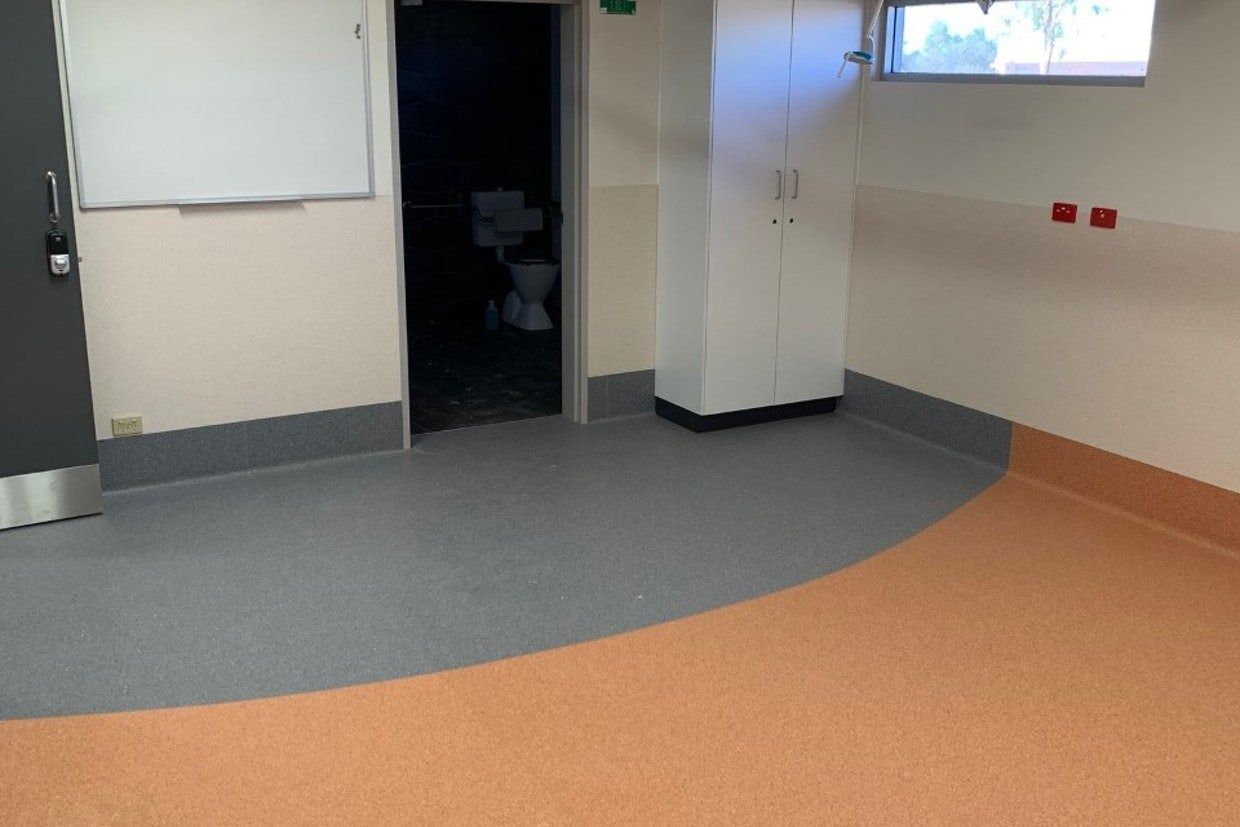 Empty Room With Grey and Orange Flooring, White Cabinets, and a Door — Ozwide Flooring In Ciccone, NT