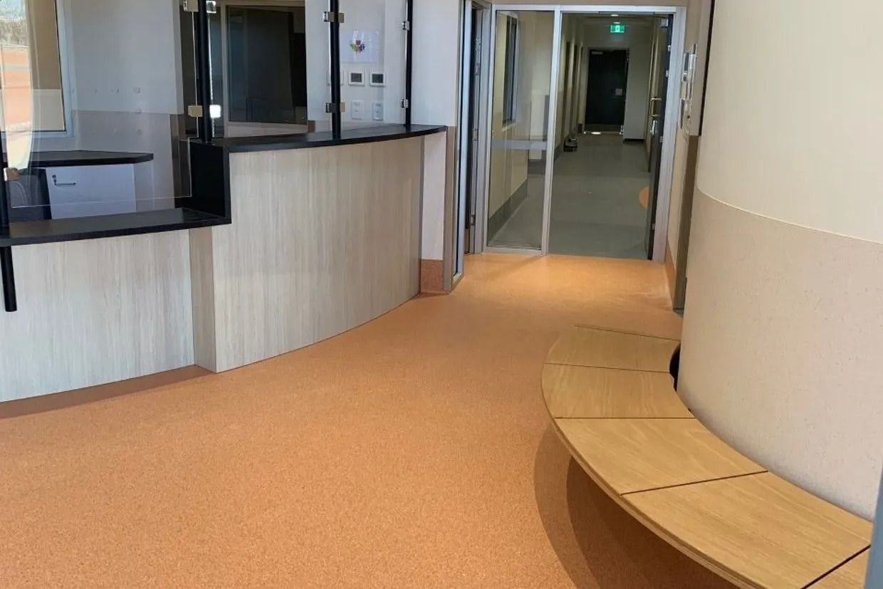 A Curved Hallway With an Orange Floor, Wooden Bench, and a Reception Desk — Ozwide Flooring In Ciccone, NT