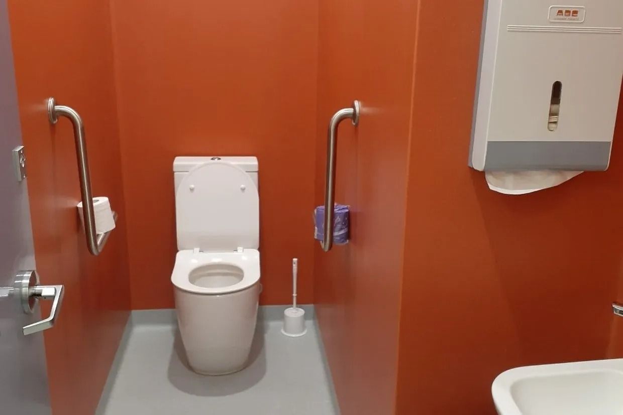 Accessible Restroom With Orange Walls, Toilet, Grab Bars, and Paper Towel Dispenser — Ozwide Flooring In Ciccone, NT