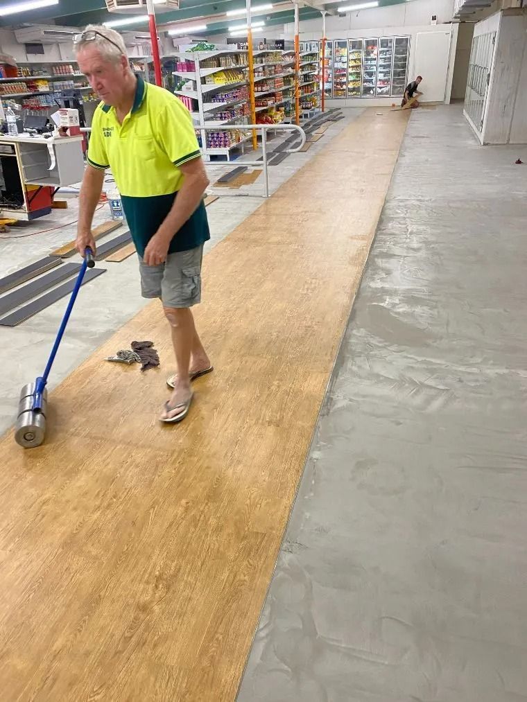 Man Rolling a Patterned Floor Covering in a Store; a Concrete Floor is Next to It — Ozwide Flooring In Ciccone, NT