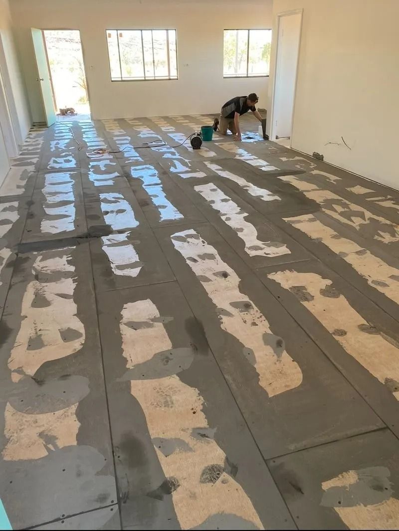 Person Installing Floor Tiles in a Bright Room With Exposed Cement Patches — Ozwide Flooring In Ciccone, NT